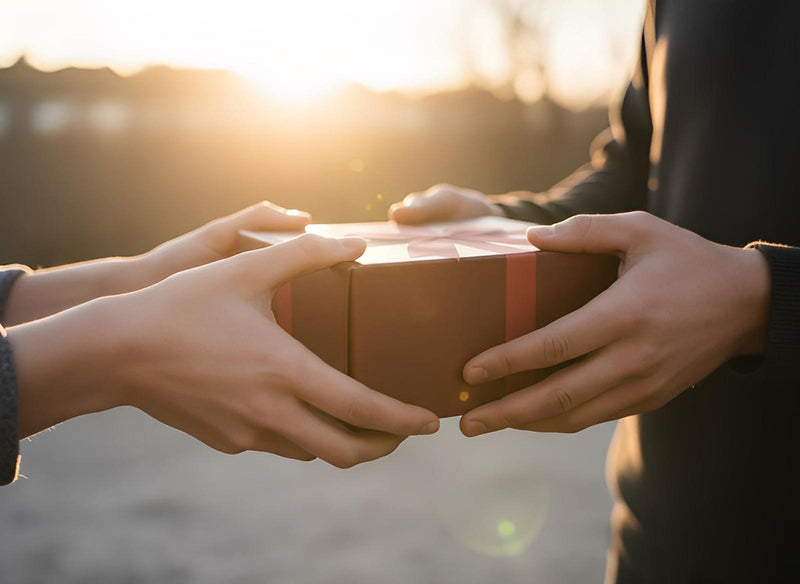 Person giving a gift box during sunset, representing friendship and thoughtful gestures for The Best Friend Candle.