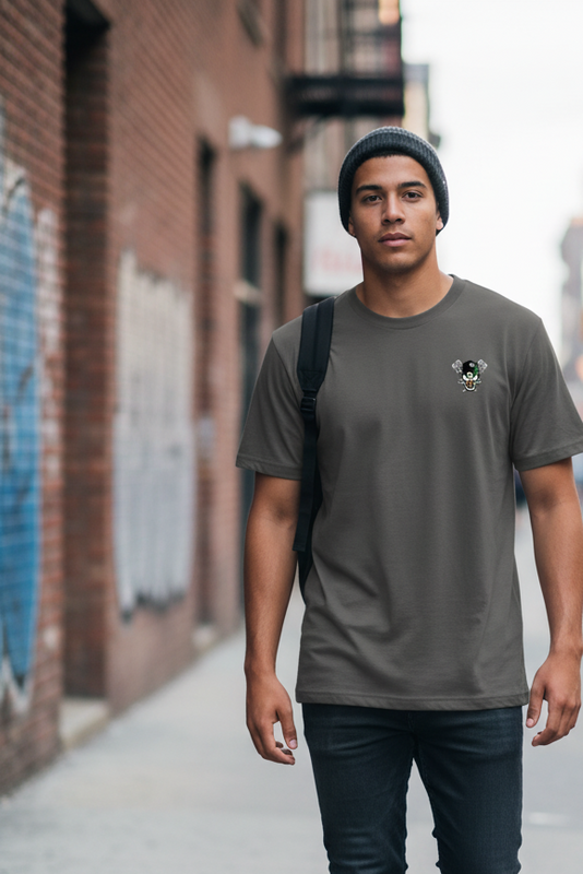 Man wearing a gray t-shirt with a logo, standing on a street with brick walls and graffiti.